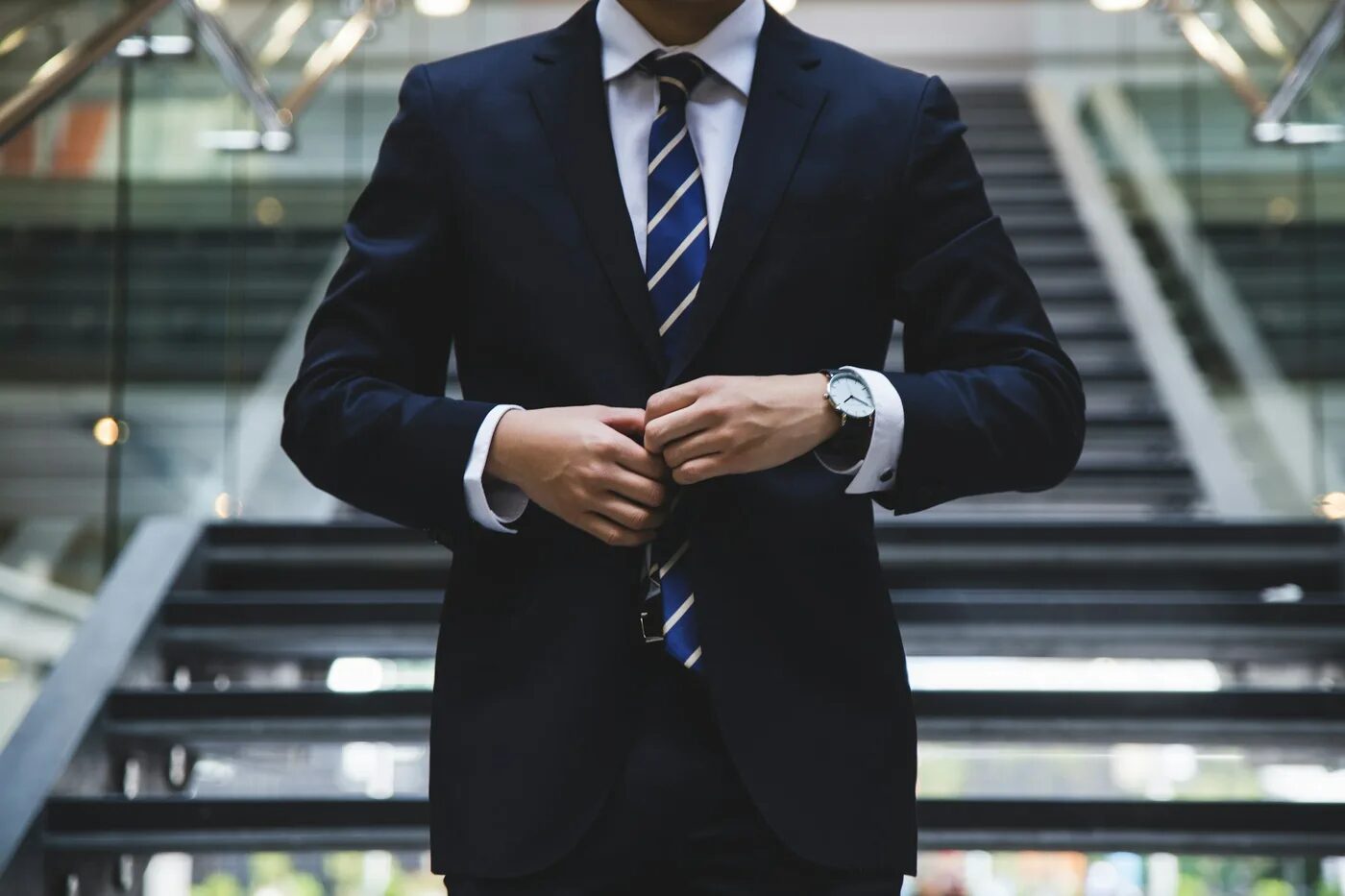 Man buttoning a navy business suit with a striped tie